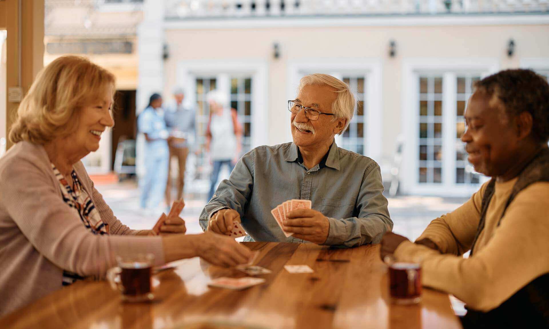 Happy Senior Man Plays Poker With His Friends At Retirement Community.